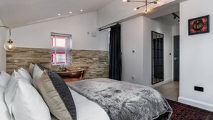 Ein modernes Schlafzimmer mit einem großen Bett, einer Wand aus Stein, einem Fenster mit Jalousien, einer schwarzen Tür und einem roten Teppich mit Muster.