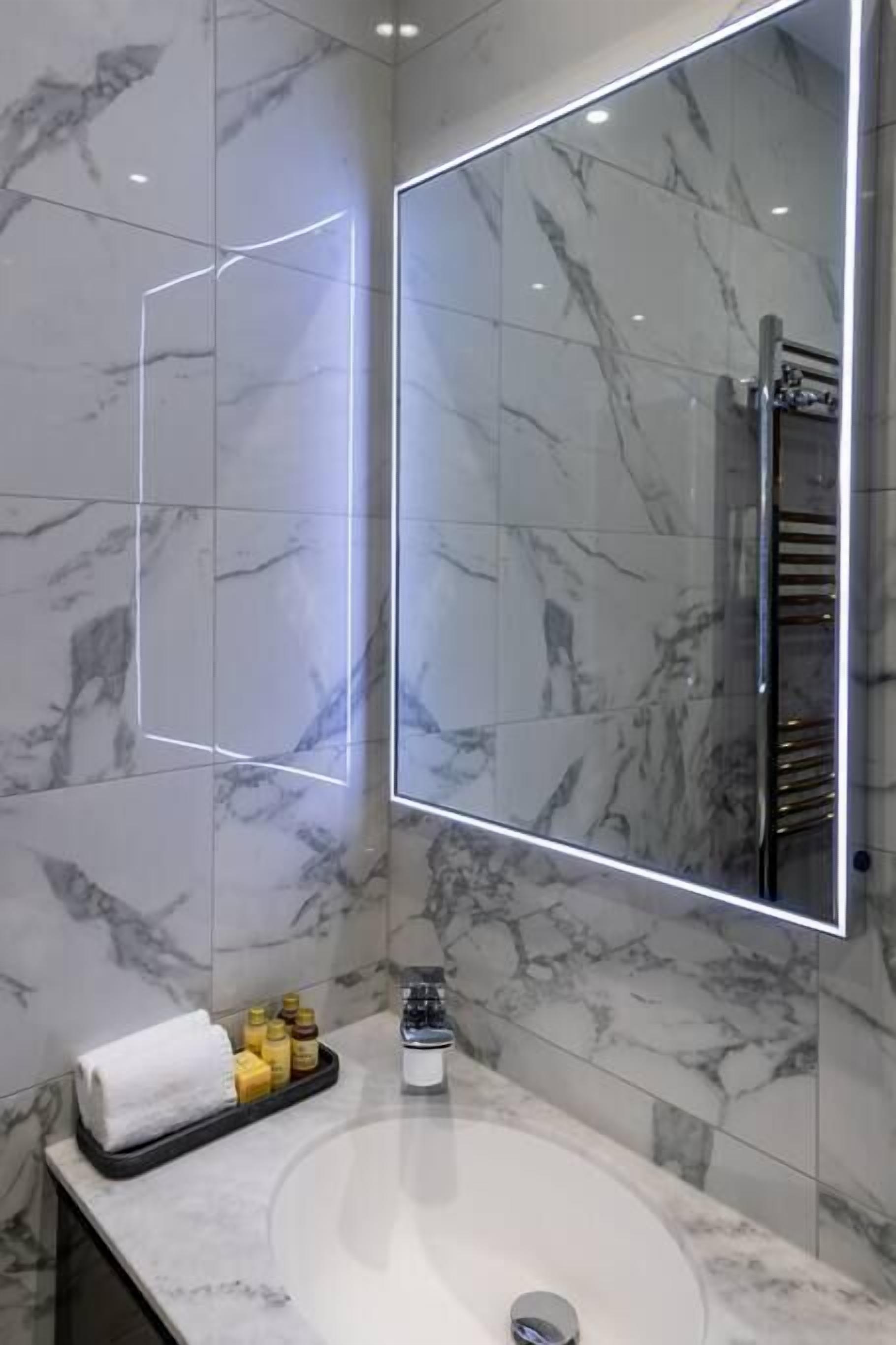 Um banheiro moderno com azulejos de mármore, um espelho grande, uma banheira e produtos de higiene no balcão.