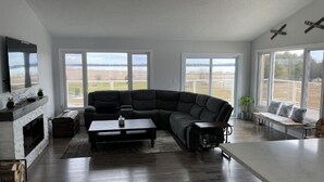 Ein geräumiges Wohnzimmer mit einer großen Eckcouch, einem Kamin und großen Fenstern mit Blick ins Freie.