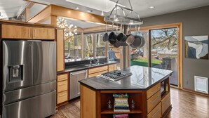 A modern kitchen with a stainless steel refrigerator, wooden cabinets, and a large island with a built-in sink.