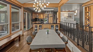A modern kitchen with wooden cabinets, a central island, and a dining area with a long table and benches.