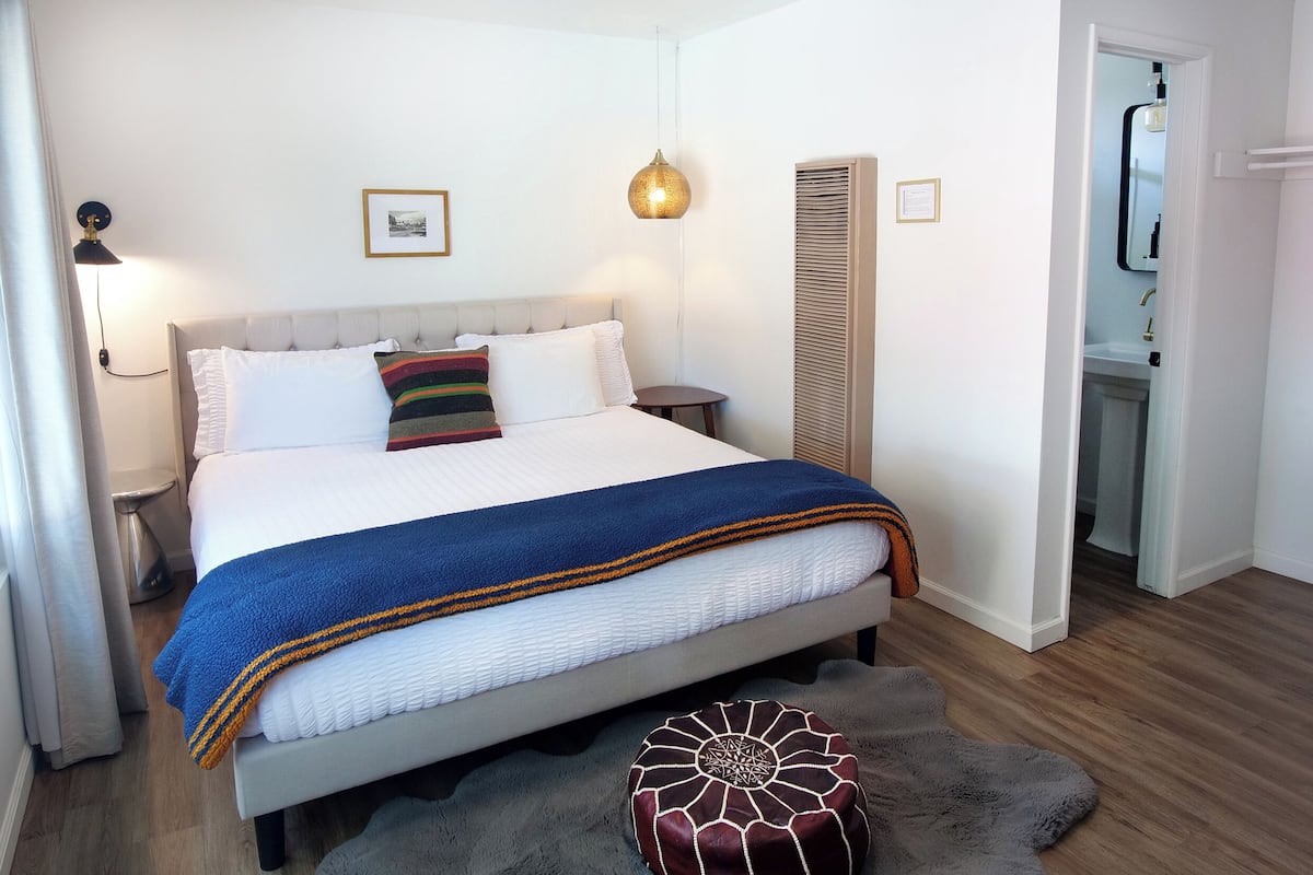 A neatly arranged bedroom with a bed, bedside tables, a ceiling fan, and a small bathroom visible through an open door.