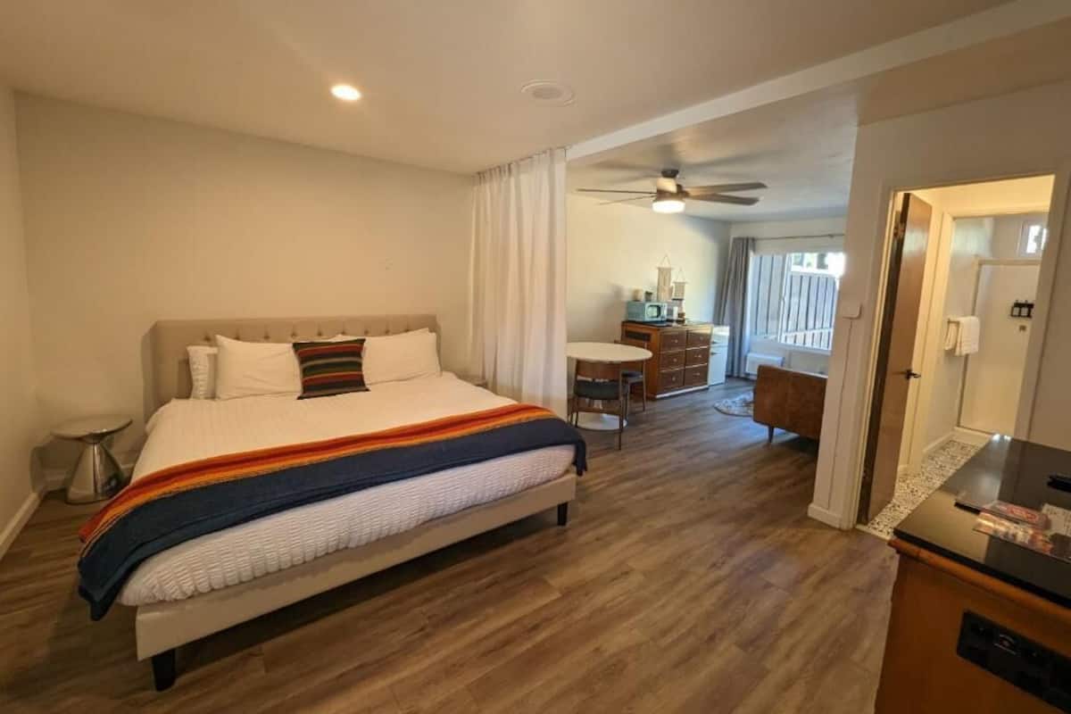 A hotel room with a large bed, a desk, a chair, and a ceiling fan.