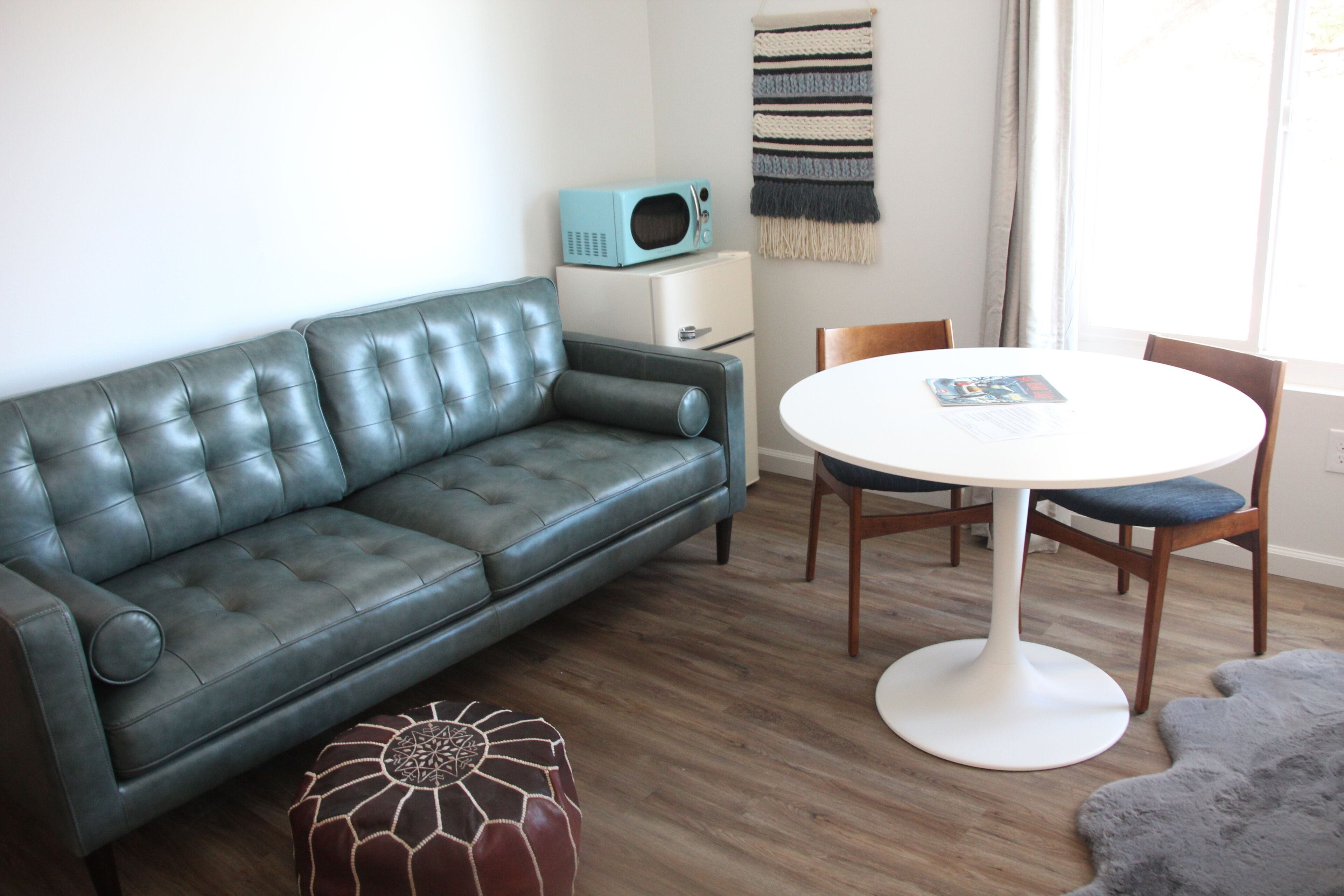 A modern living room with a dark leather sofa, a white round table, and a small white cabinet.