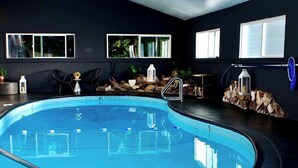 Une piscine intérieure à l’eau claire, entourée d’un mur sombre percé de fenêtres.