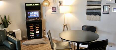 Uma sala de estar moderna com um console de jogos, uma mesa de jantar redonda e um arranjo de assentos confortável.