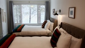 Une chambre d’hôtel avec deux lits, une grande fenêtre avec des rideaux, une lampe fixée au mur et un tableau encadré.