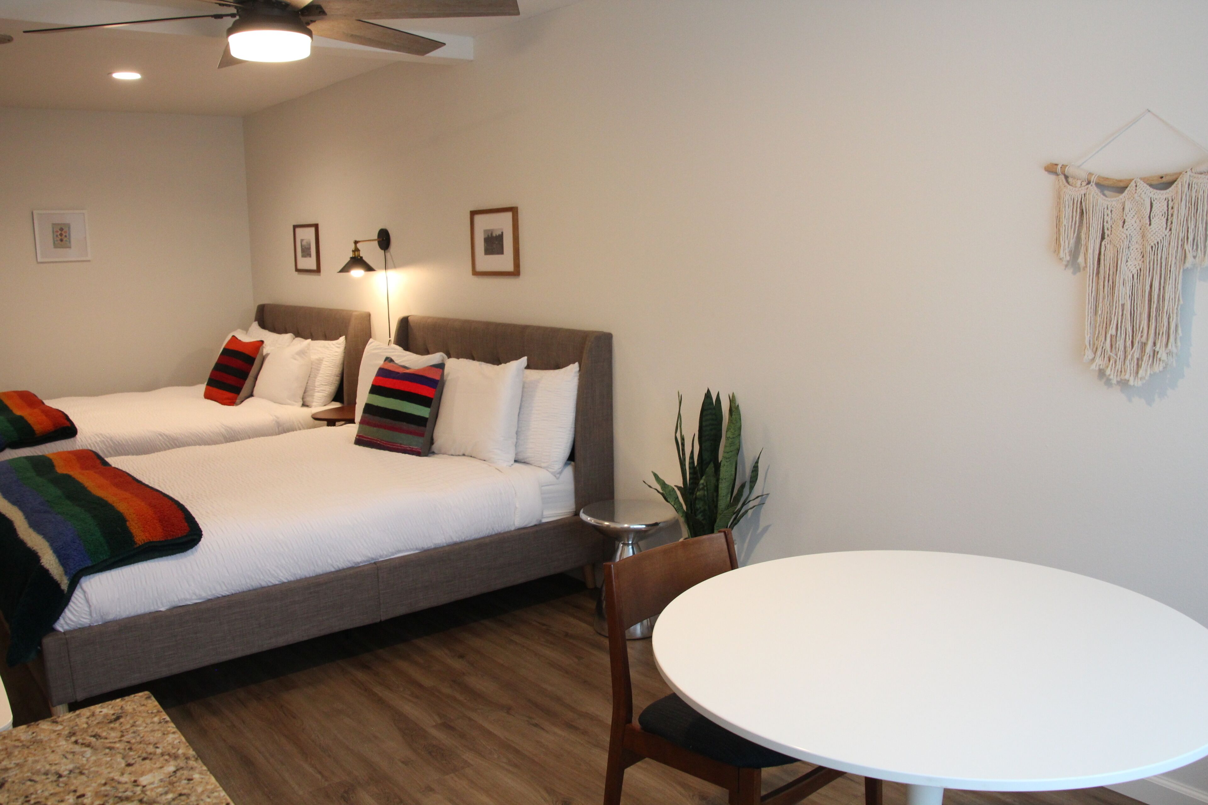 A hotel room with two beds, a round table, and a ceiling fan.