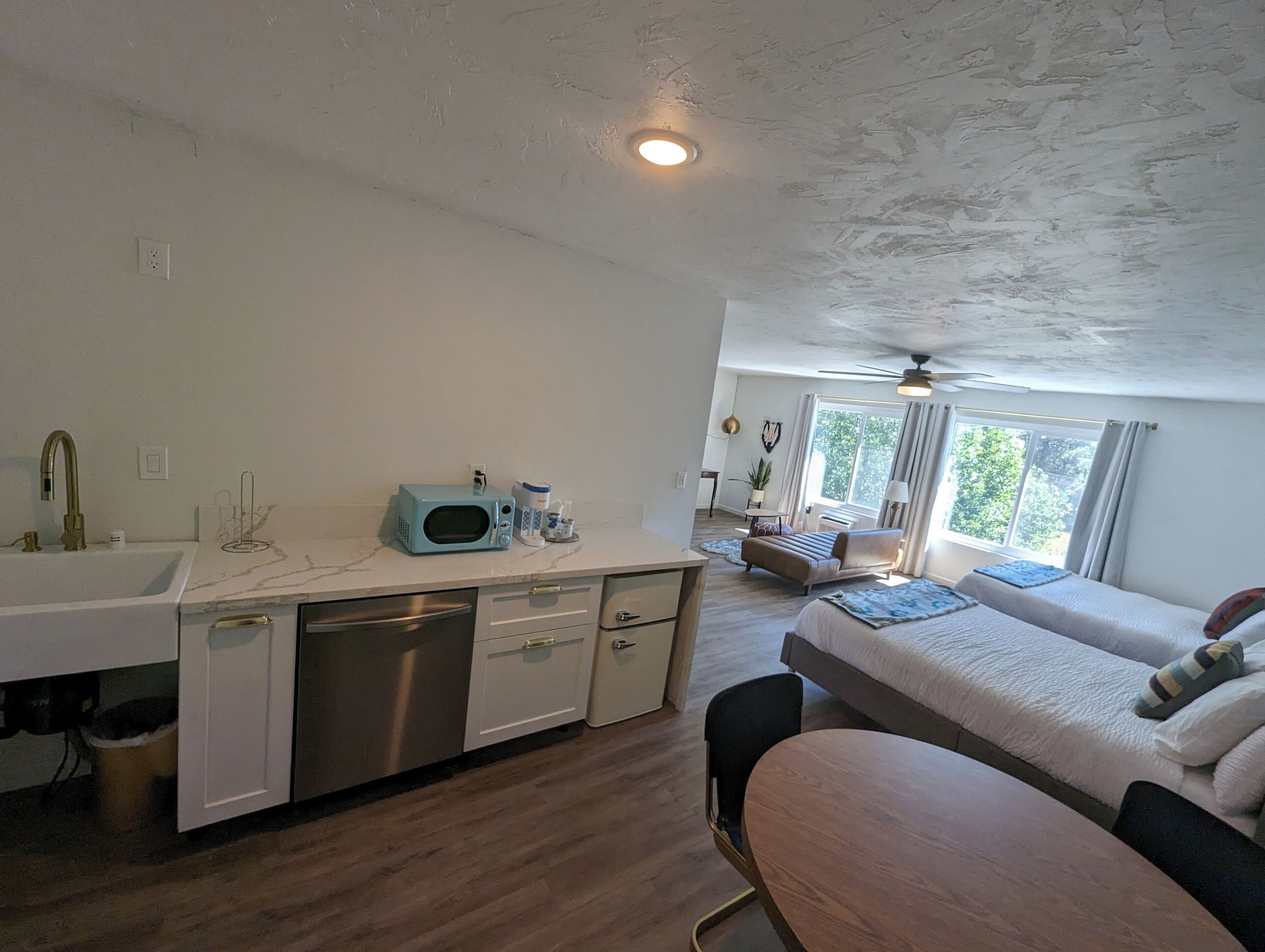 Een compacte kamer met kitchenette, een eettafel, een bank en een raam met uitzicht op groen.