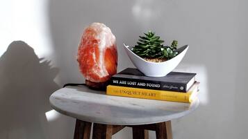 Una lámpara de sal, una planta suculenta y dos libros sobre una mesita de madera frente a una pared lisa.