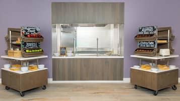 Un espace cuisine doté d’un îlot central, de deux chariots de service mobiles placés de part et d’autre, et de panneaux noirs indiquant les plats disponibles.