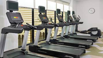 En rad löpband med digitala displayer, placerade i ett gym med stora fönster och en klocka på väggen.