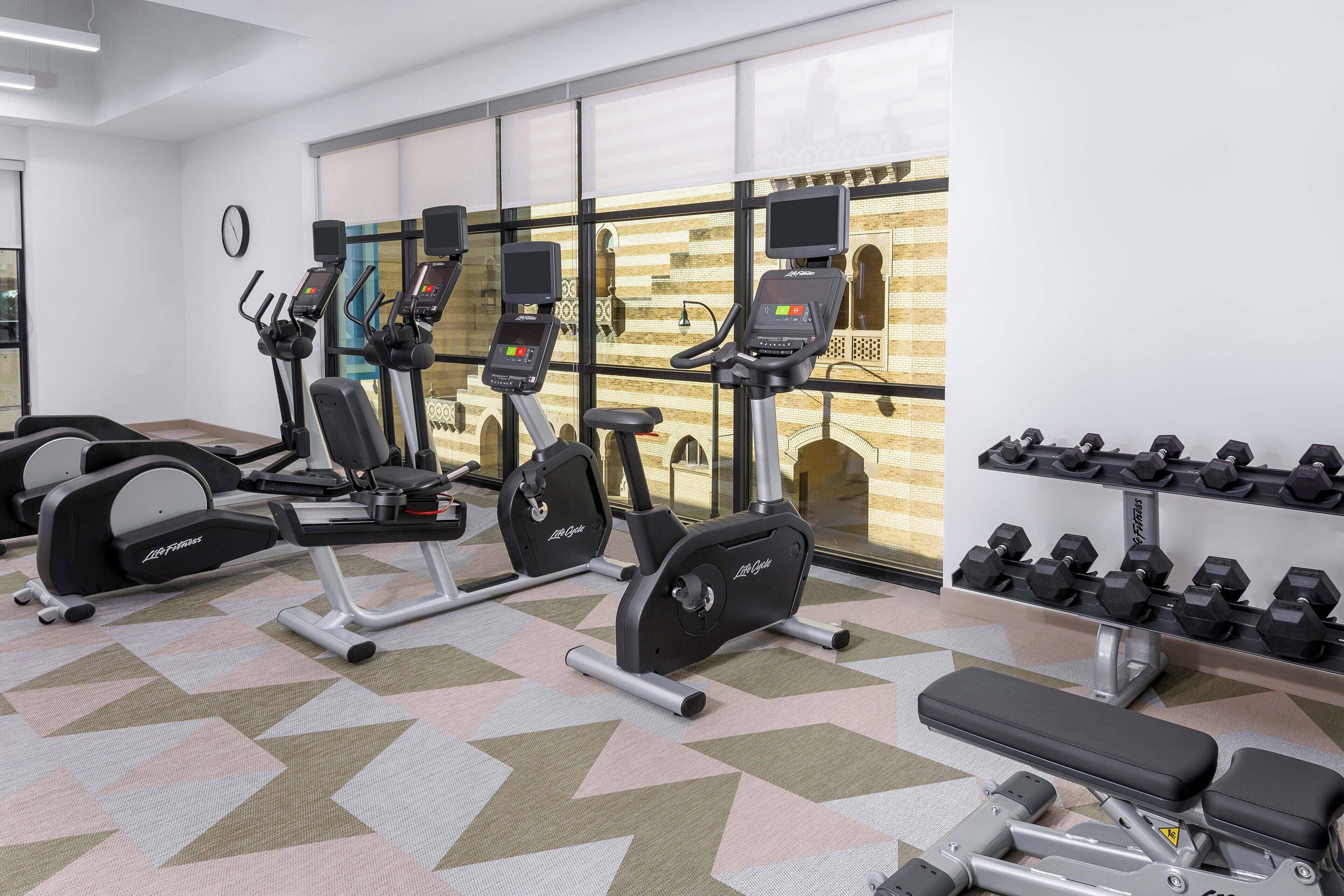 A gym with cardio machines, dumbbells, and a bench.