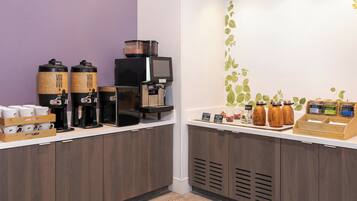 Un espace dédié au café, équipé de plusieurs machines à café, où sont exposés différents types de grains de café, et où un panneau indique la possibilité d’obtenir du café gratuitement.