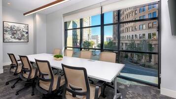 Uma sala de conferência com uma mesa grande, seis cadeiras e vista para a paisagem urbana através de grandes janelas.