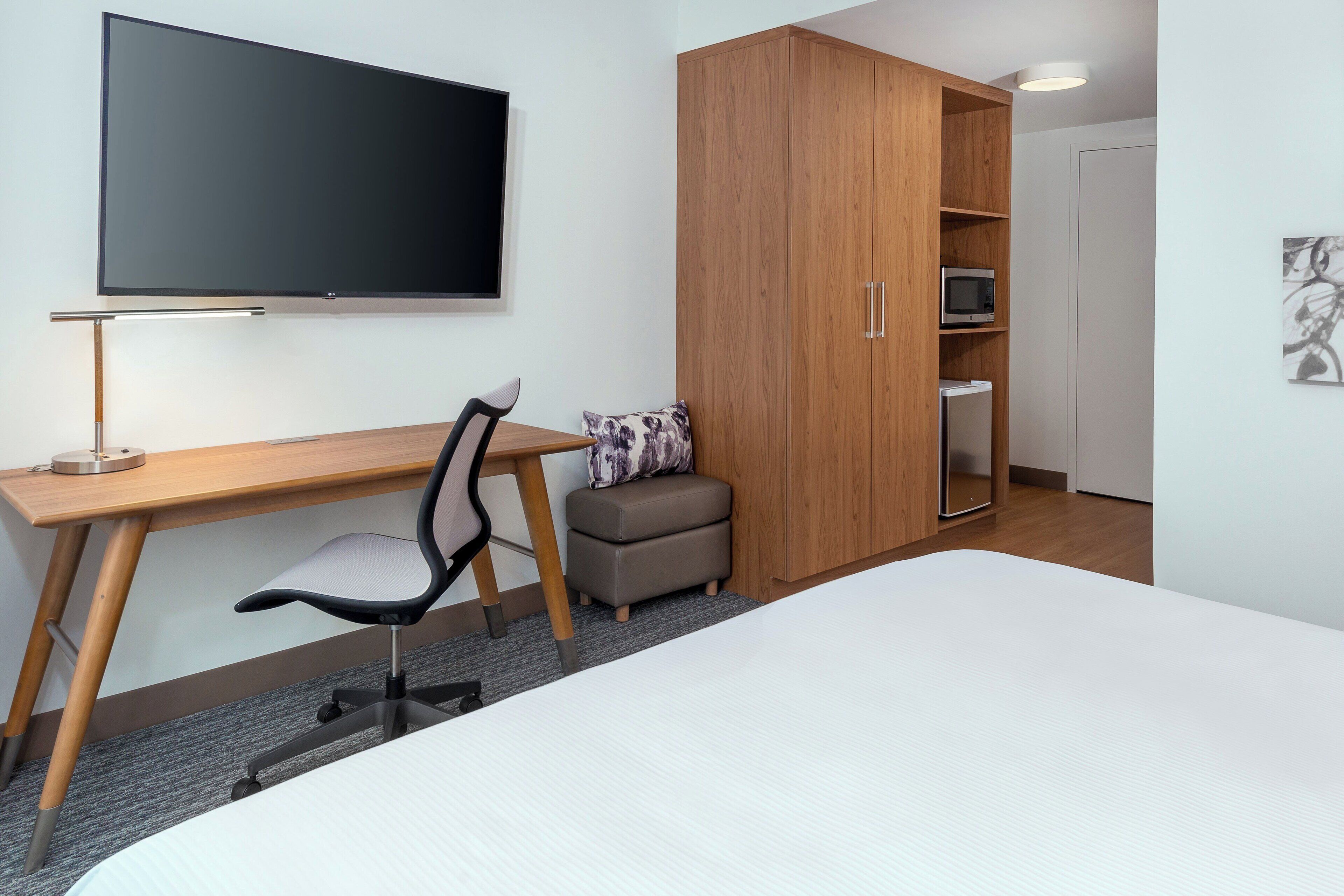 Ein Hotelzimmer mit einem Bett, einem Schreibtisch mit Stuhl, einem Fernseher, einem Kleiderschrank und einer Mikrowelle.
