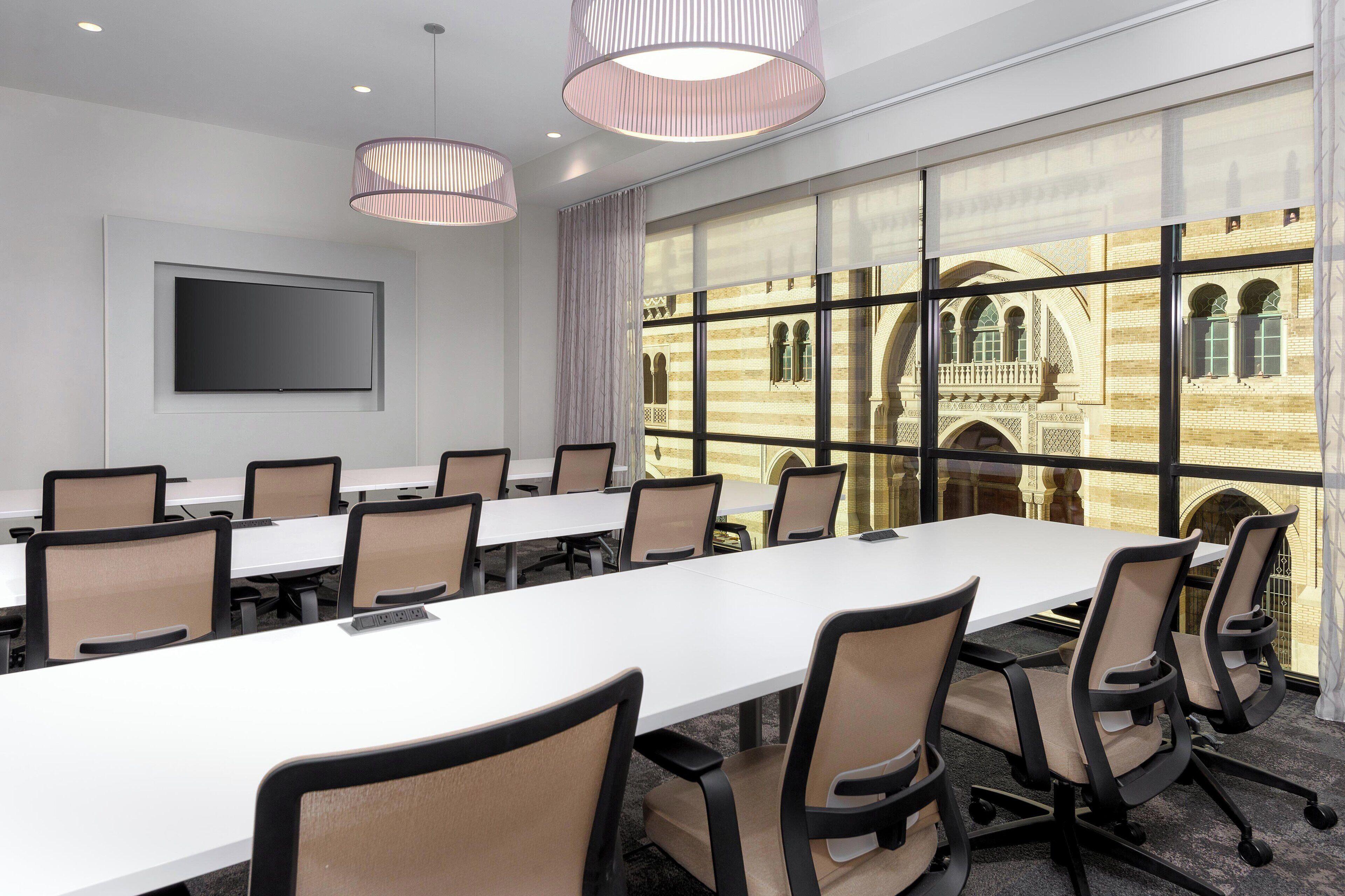 A conference room with a long table, chairs, a TV, and large windows with a view of historic architecture.