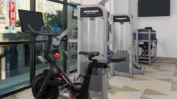 Uma academia interna com equipamentos de exercícios, incluindo uma bicicleta ergométrica, um aparelho de puxada alta e um aparelho de supino.