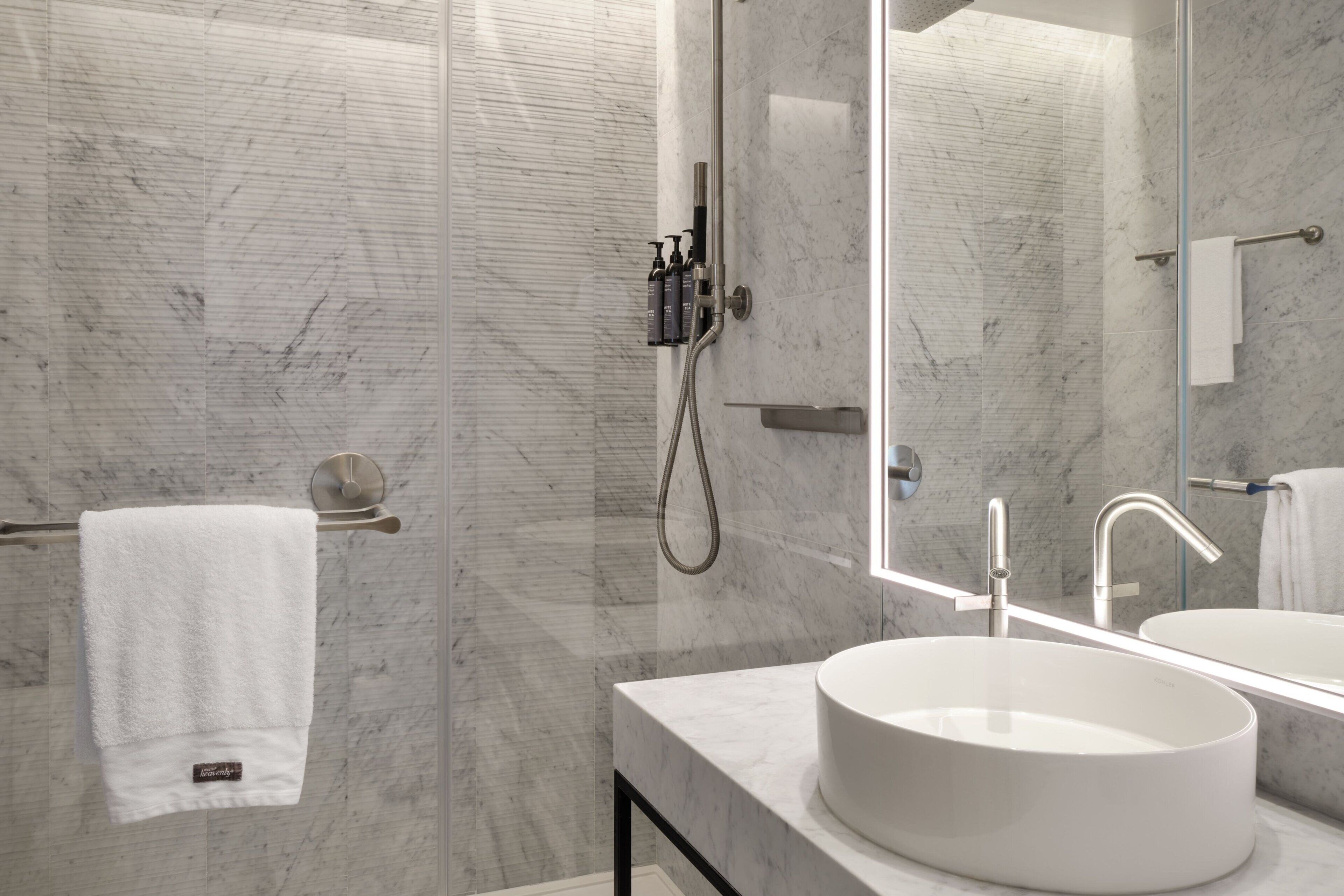 A modern bathroom with a large mirror, a round sink, and a shower with a handheld showerhead.