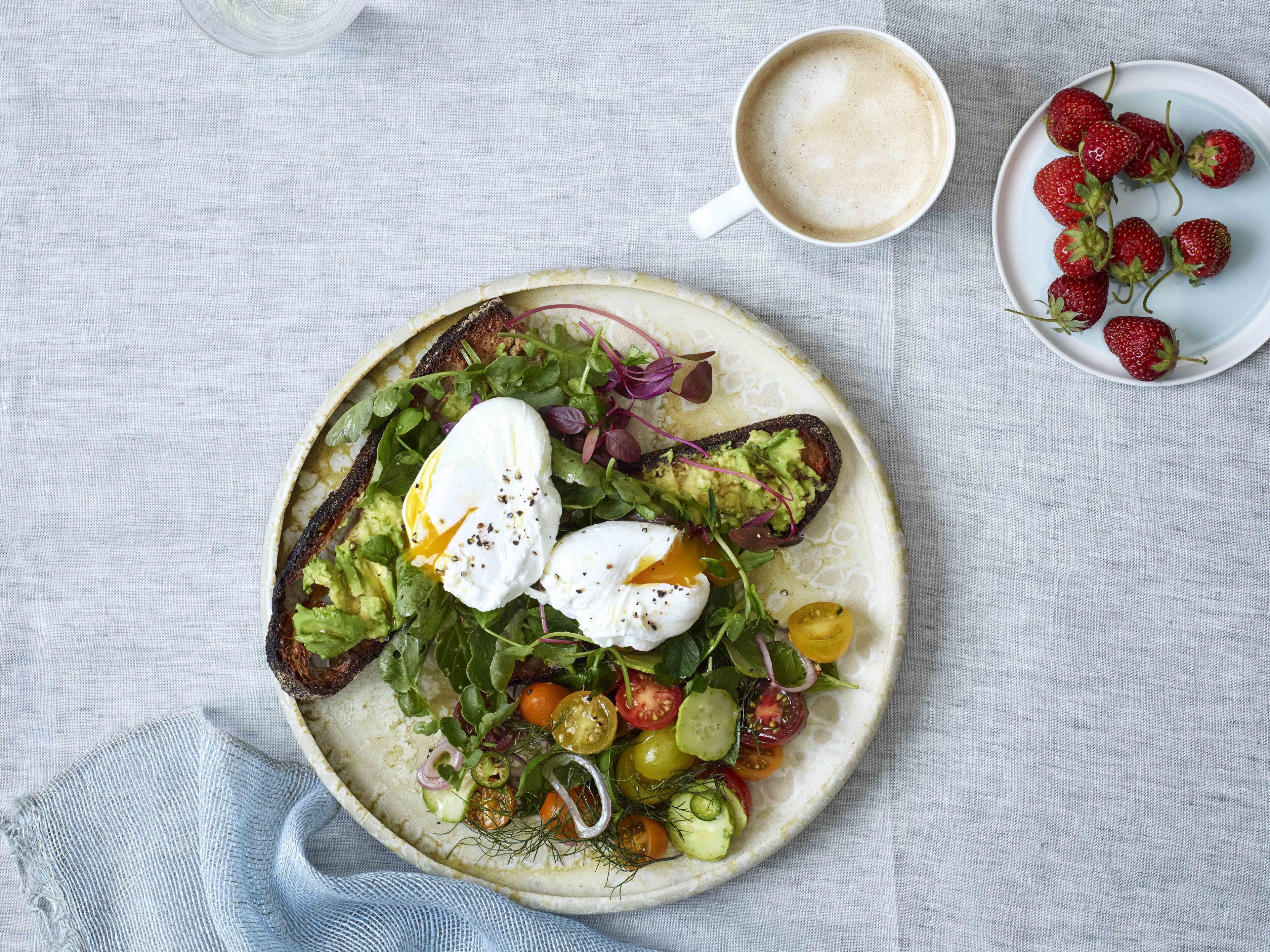 A plate of food with a poached egg, avocado, greens, and cherry tomatoes on a round plate.