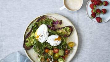 A plate of food with a poached egg, avocado, greens, and cherry tomatoes on a round plate.