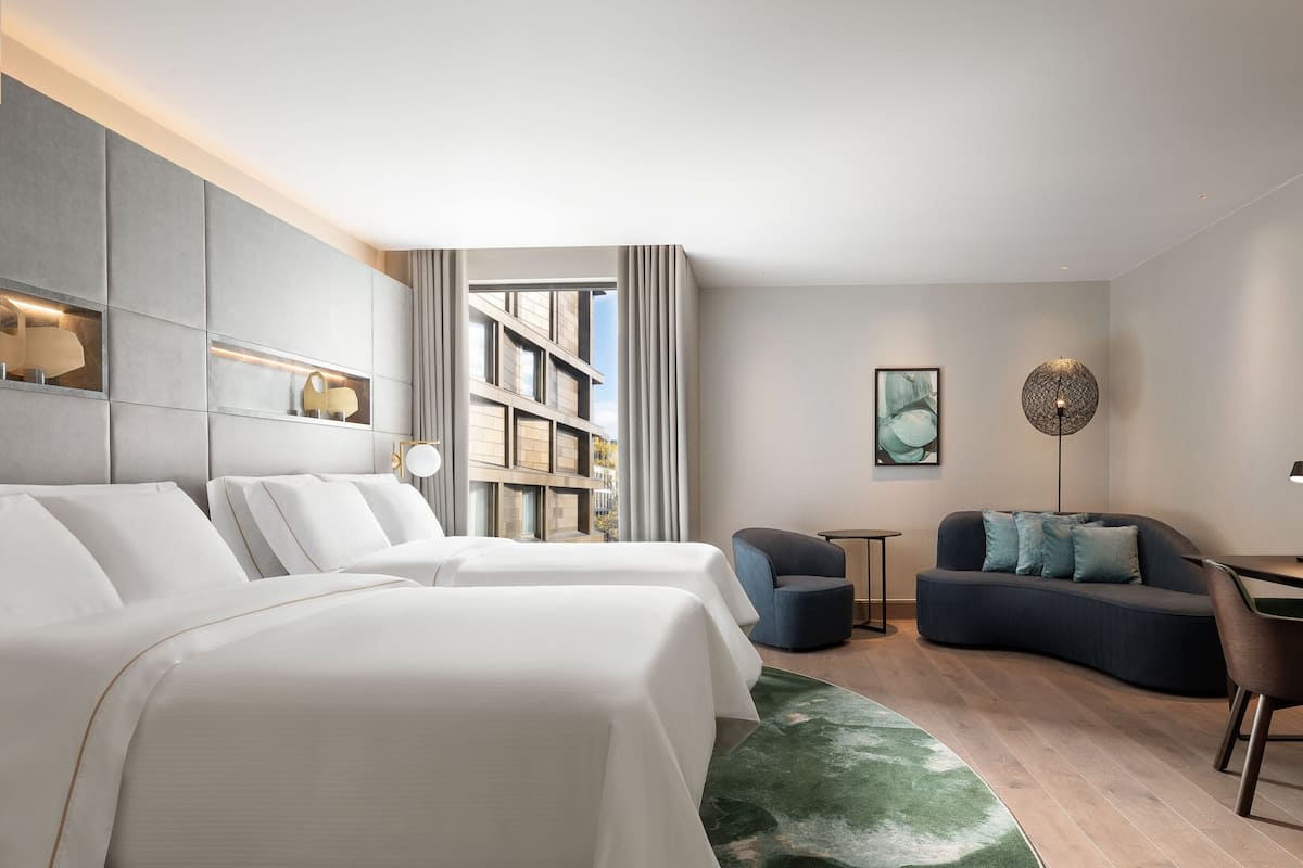 Habitació d'hotel moderna amb dos llits, un sofà, una taula petita i una prestatgeria.