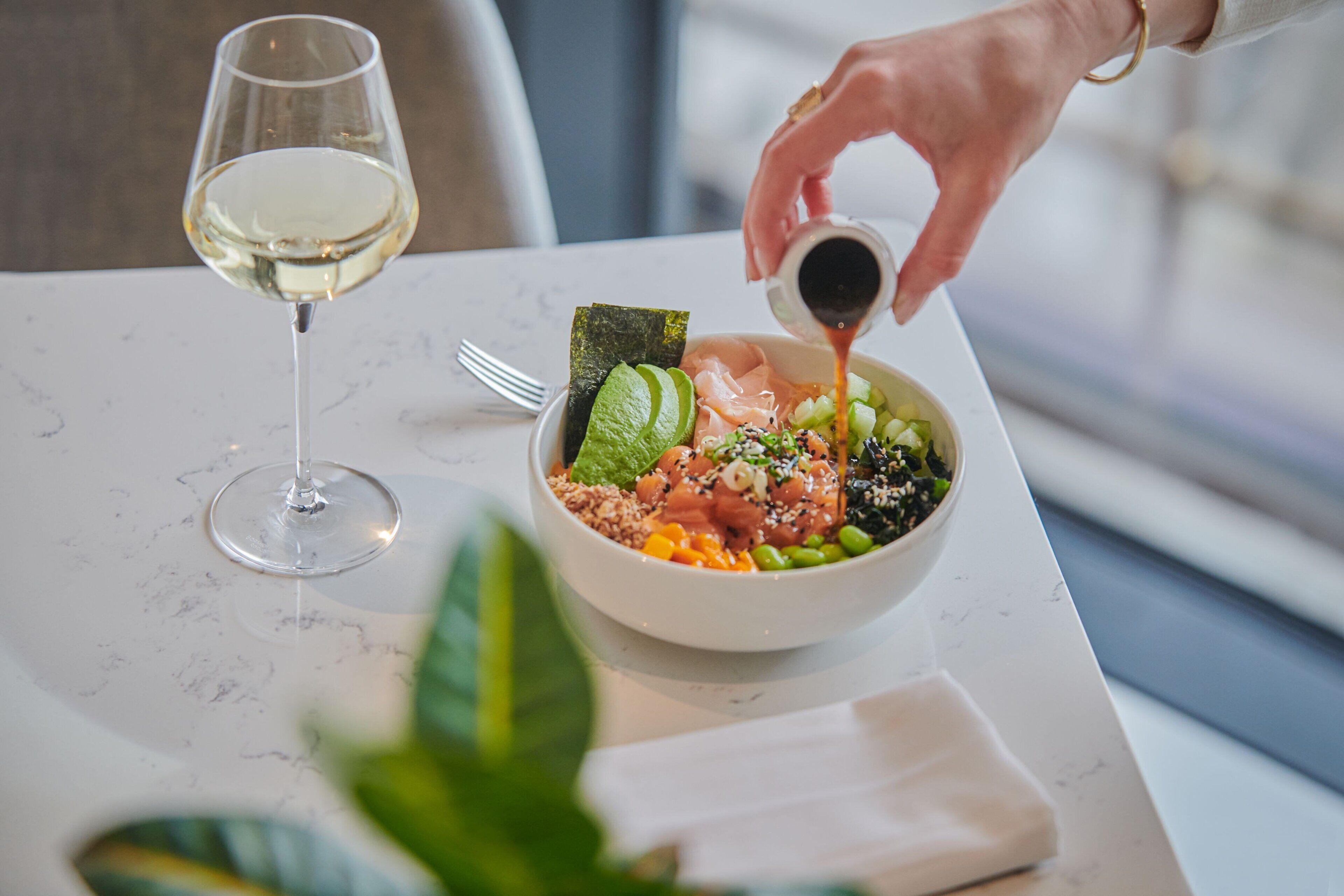 A bowl of food on a table with a glass of white wine beside it.