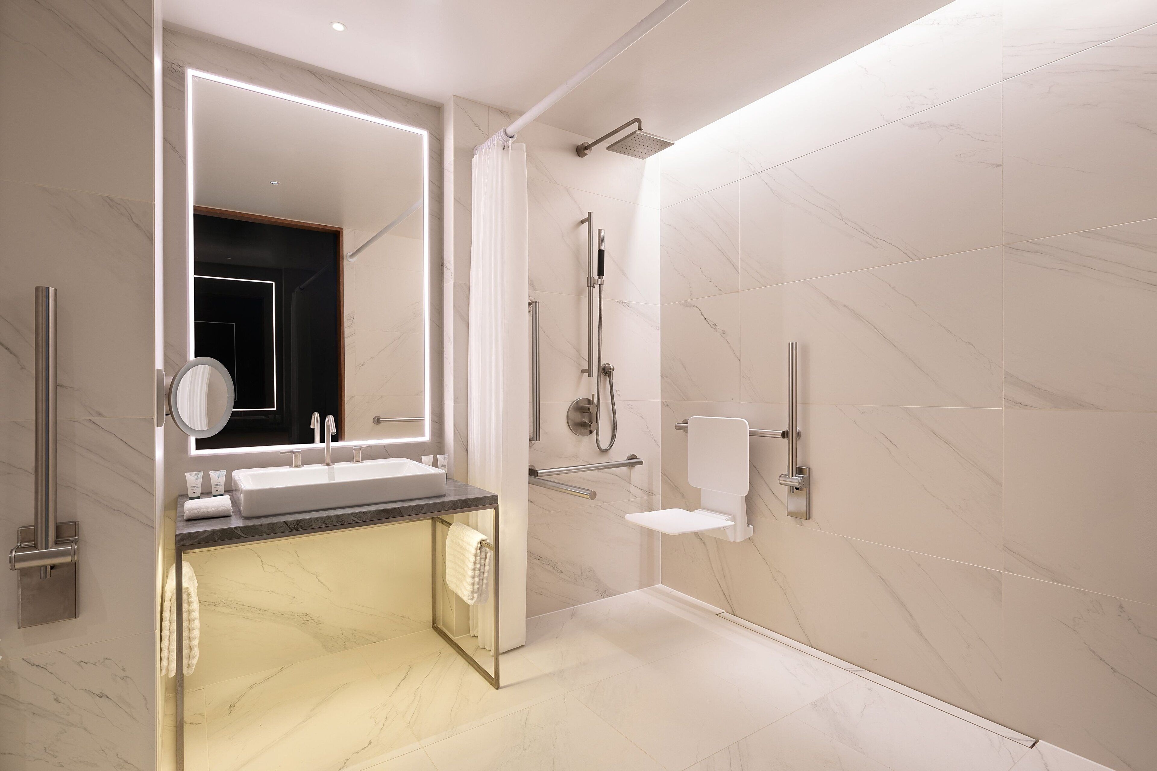 A modern bathroom with a large mirror, a sink, a shower, and a toilet.