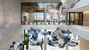 Un vaste atrium agrémenté d’œuvres d’art moderne, de grandes fenêtres offrant une vue sur la ville et d’un espace détente avec des meubles contemporains.