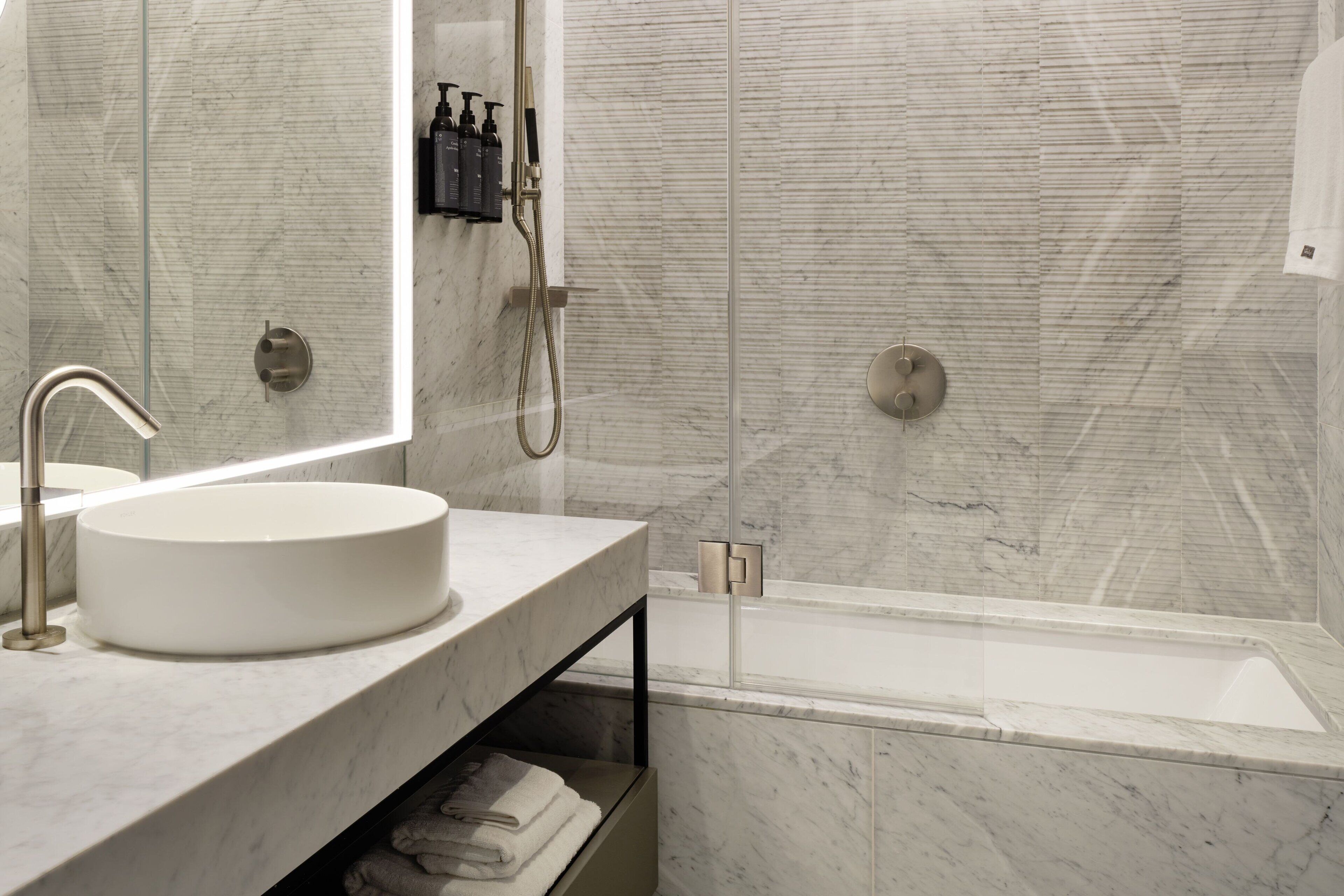 Ein modernes Badezimmer mit einem Marmorwaschbecken, einer Glaskabine zur Dusche und einer Badewanne.