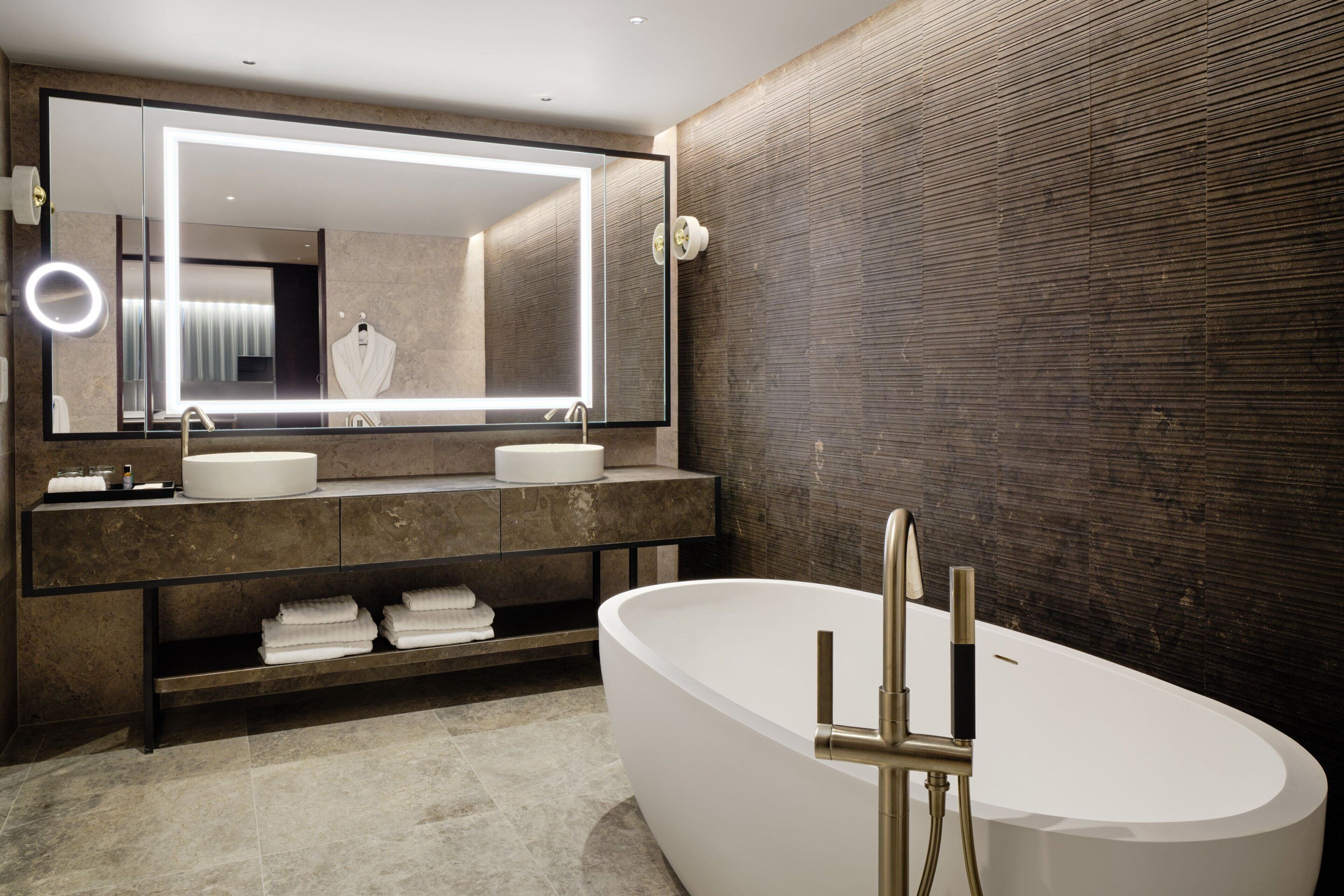 Un baño moderno con una bañera independiente, un espejo grande con iluminación integrada y un mueble de tocador con dos lavabos.