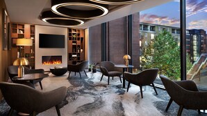 Un salon moderne doté d’une cheminée, de sièges confortables et de grandes fenêtres offrant une vue sur la ville.