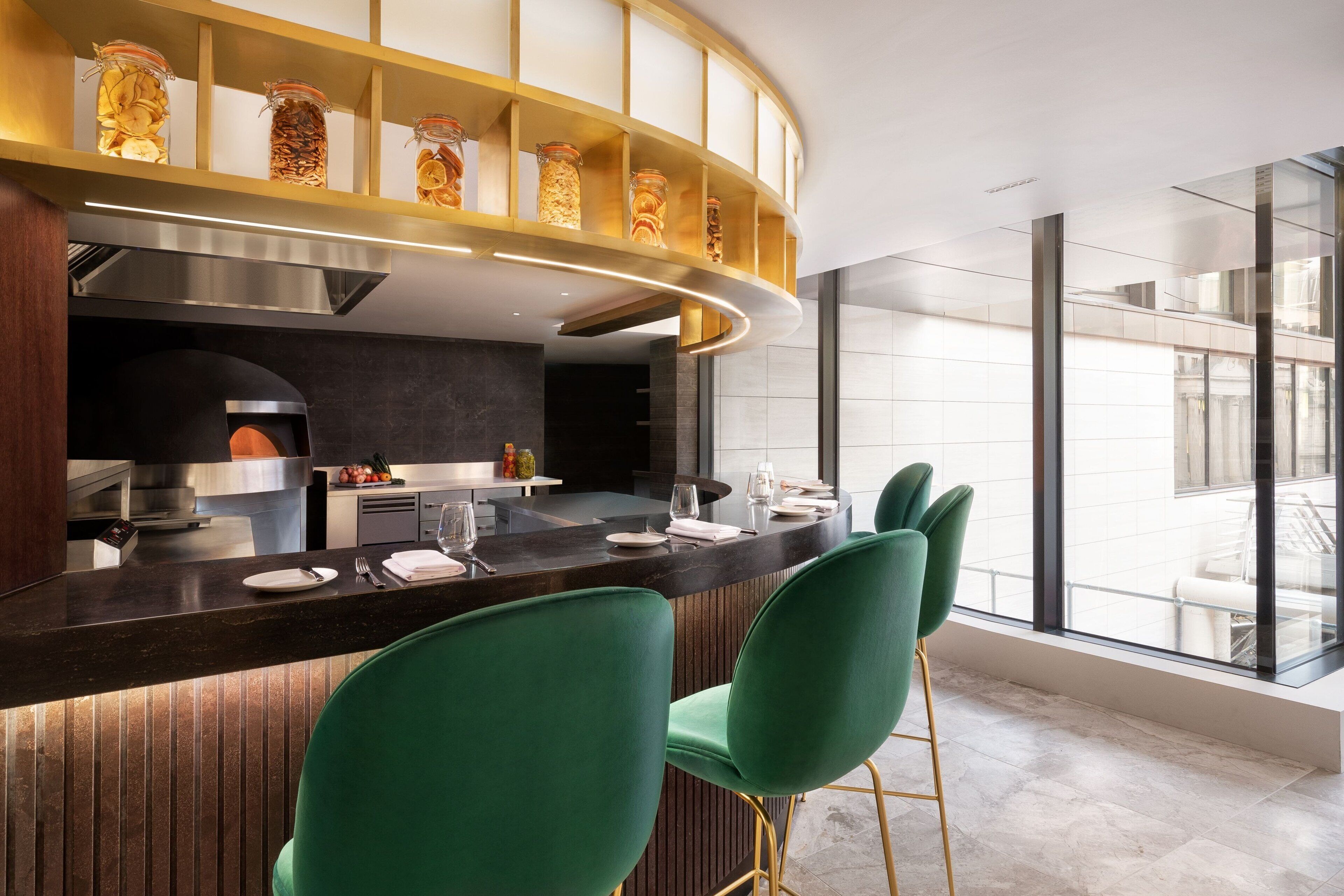 A modern kitchen with a curved island, green bar stools, and a view of the city through large windows.