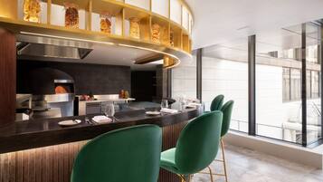 A modern kitchen with a curved island, green bar stools, and a view of the city through large windows.