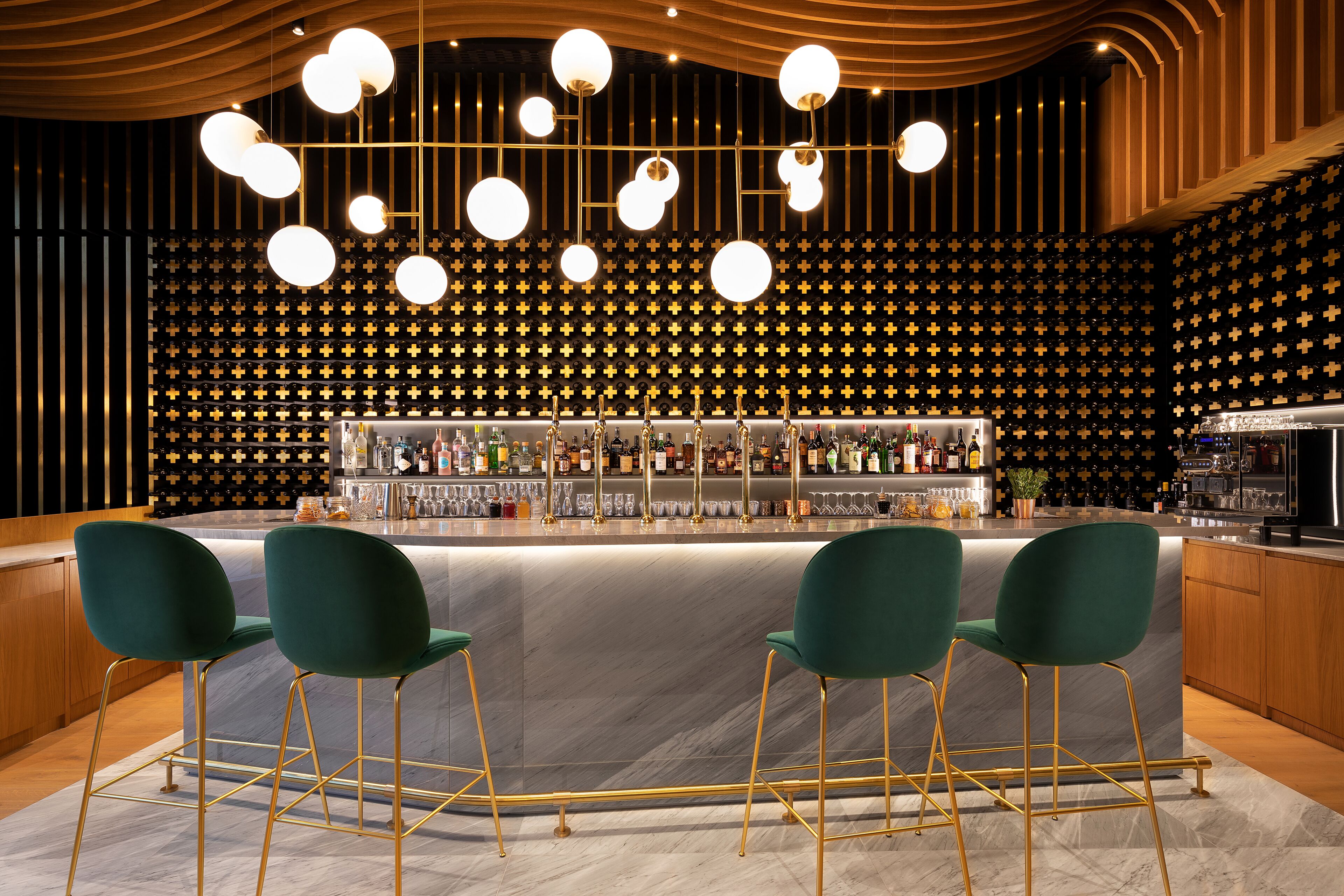Eine Bar mit Marmorplatte, grünen Barhocker und einer Wand mit Muster im Hintergrund.