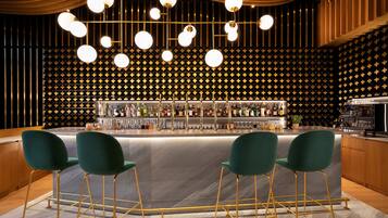 Un'area bar con un bancone in marmo, sgabelli verdi e una parete decorata sullo sfondo.