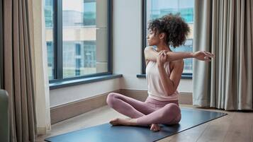 Una persona sentada sobre una colchoneta de yoga en una habitación con un ventanal y cortinas.