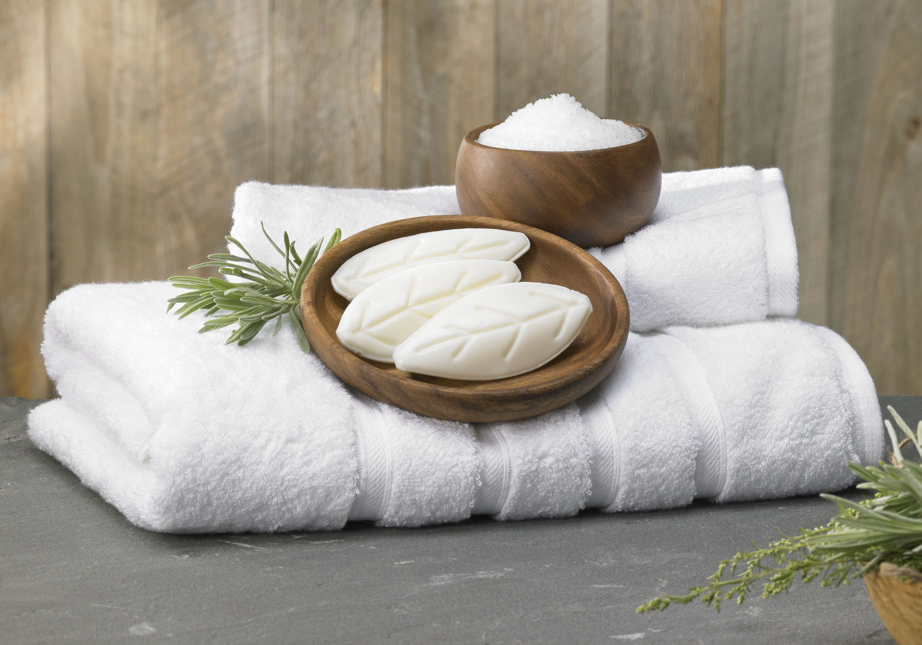 A white towel, a wooden bowl with white cubes, and a wooden bowl of white crystals on a grey surface.