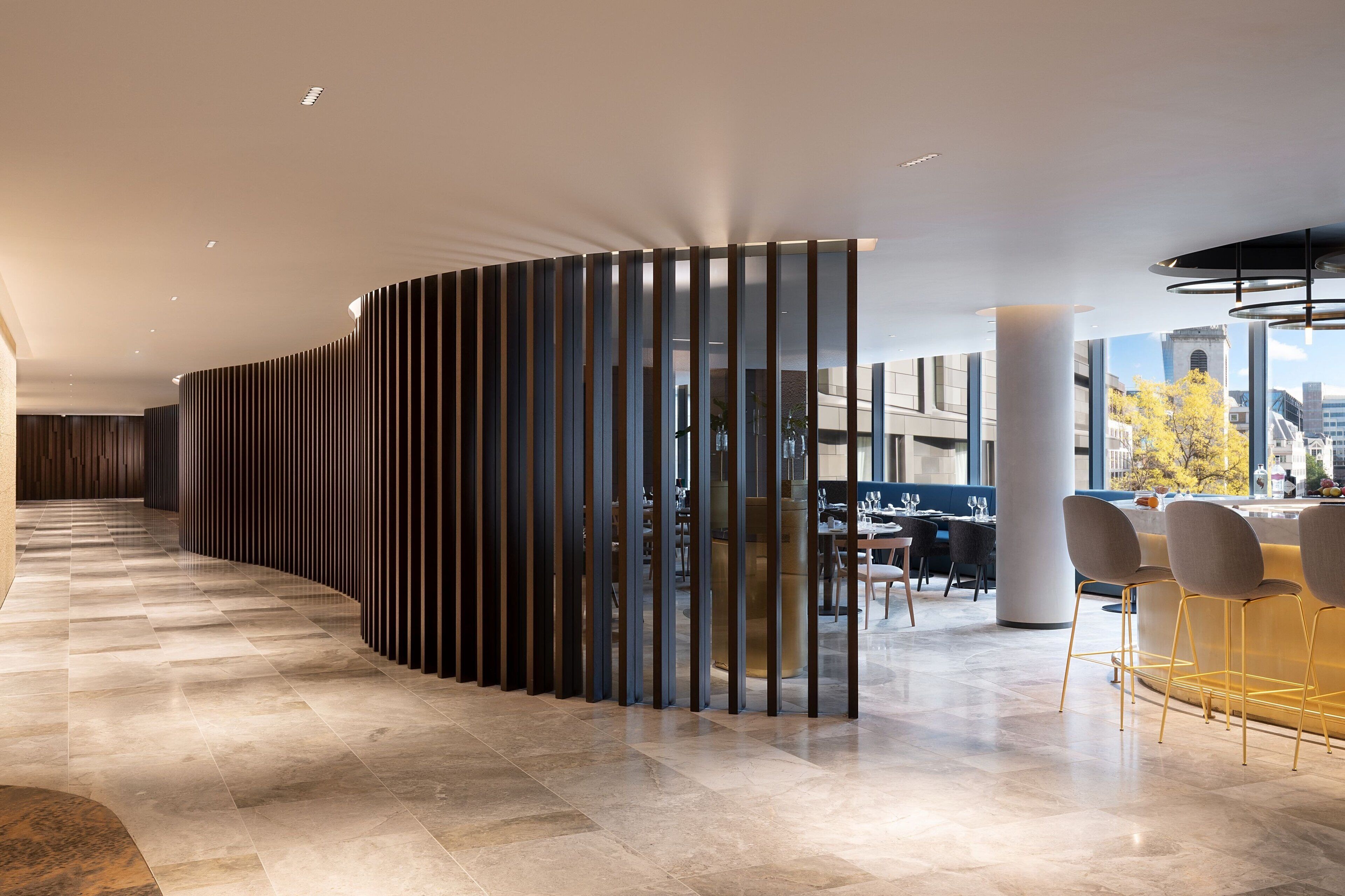 Un moderno vestíbulo de hotel con un mostrador de recepción curvo, una zona de estar con sillones y vistas a la ciudad a través de grandes ventanales.