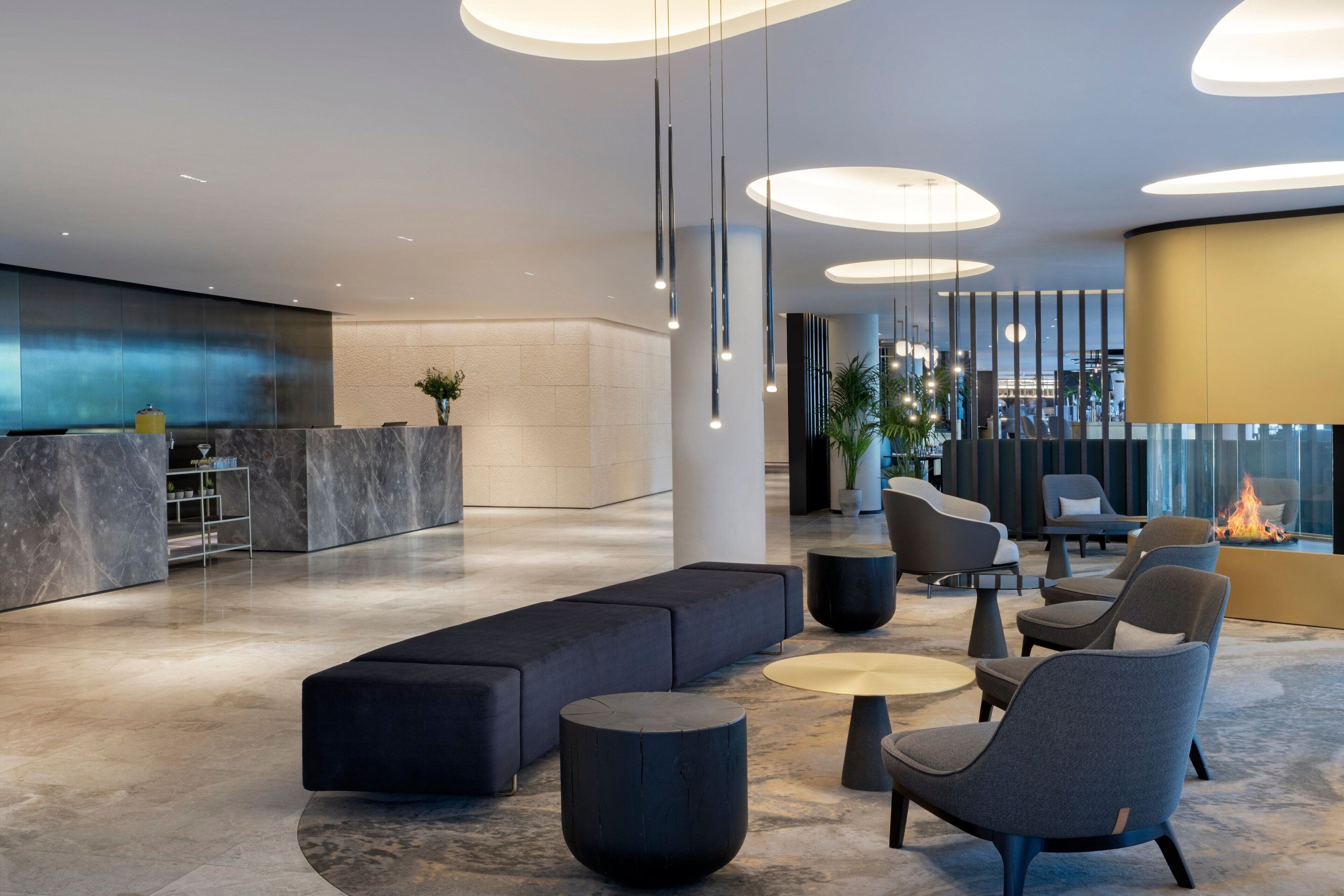 A modern lobby with a reception desk, seating area, and a fire feature.