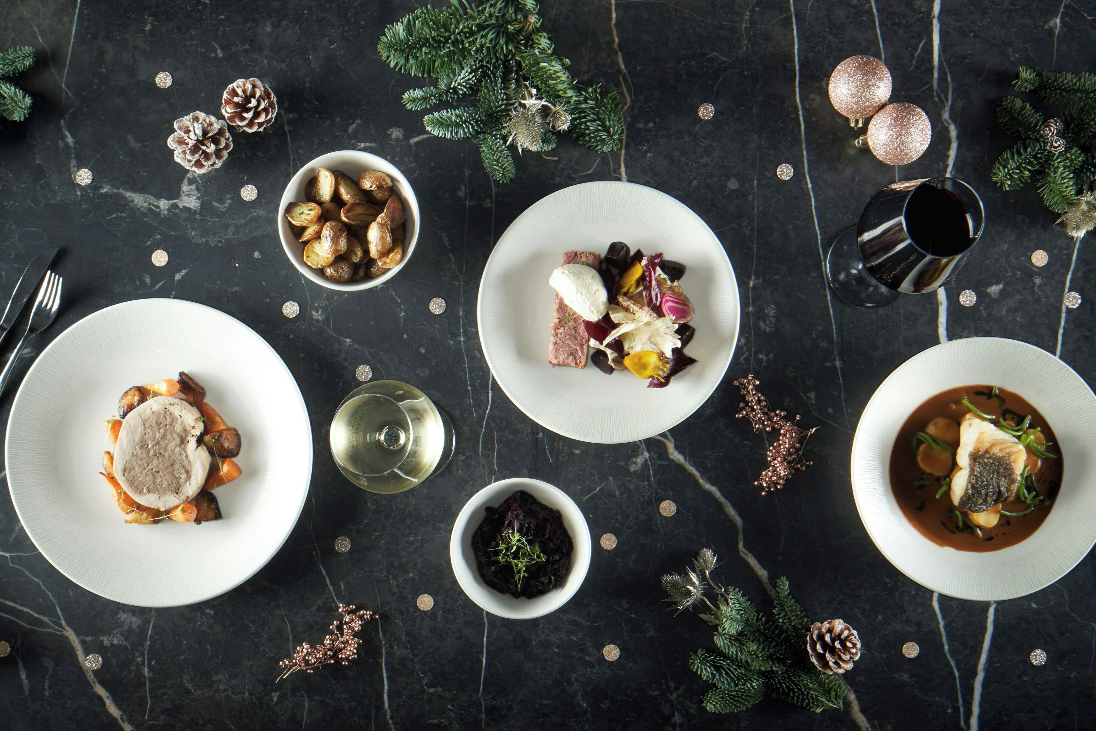 Una mesa de comedor con varios platos de comida, una copa de vino y elementos decorativos como piñas y adornos.