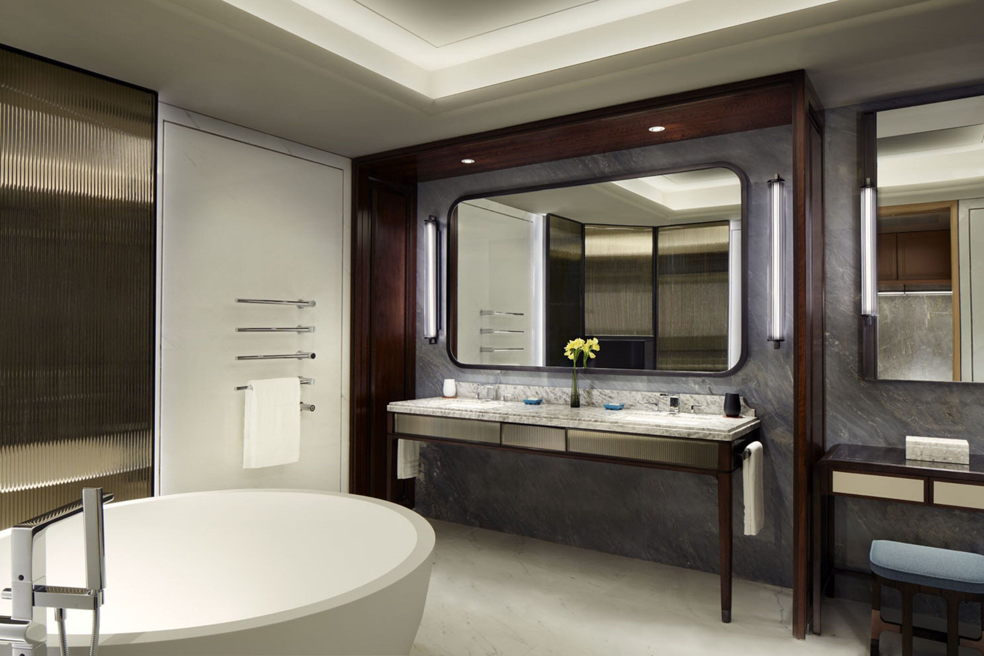 A modern bathroom with a freestanding bathtub, a large mirror, and a vanity with a marble countertop.