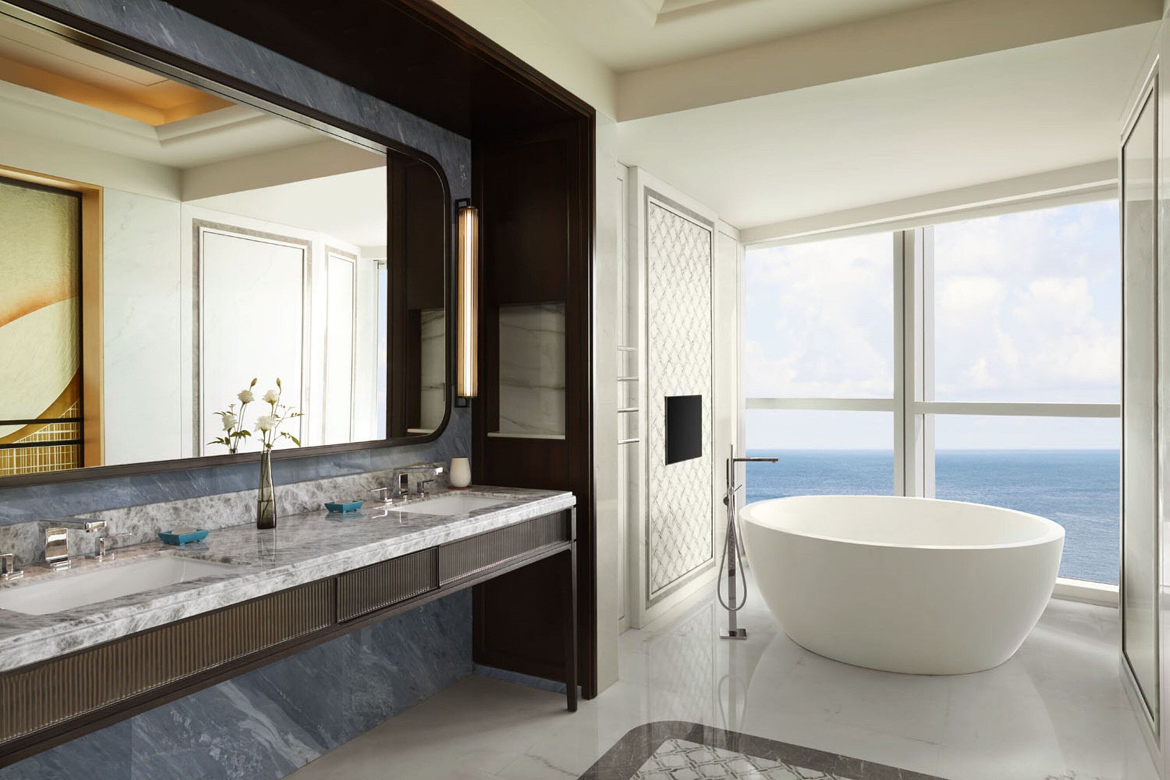 A modern bathroom with a large bathtub, a marble vanity, and a large mirror.