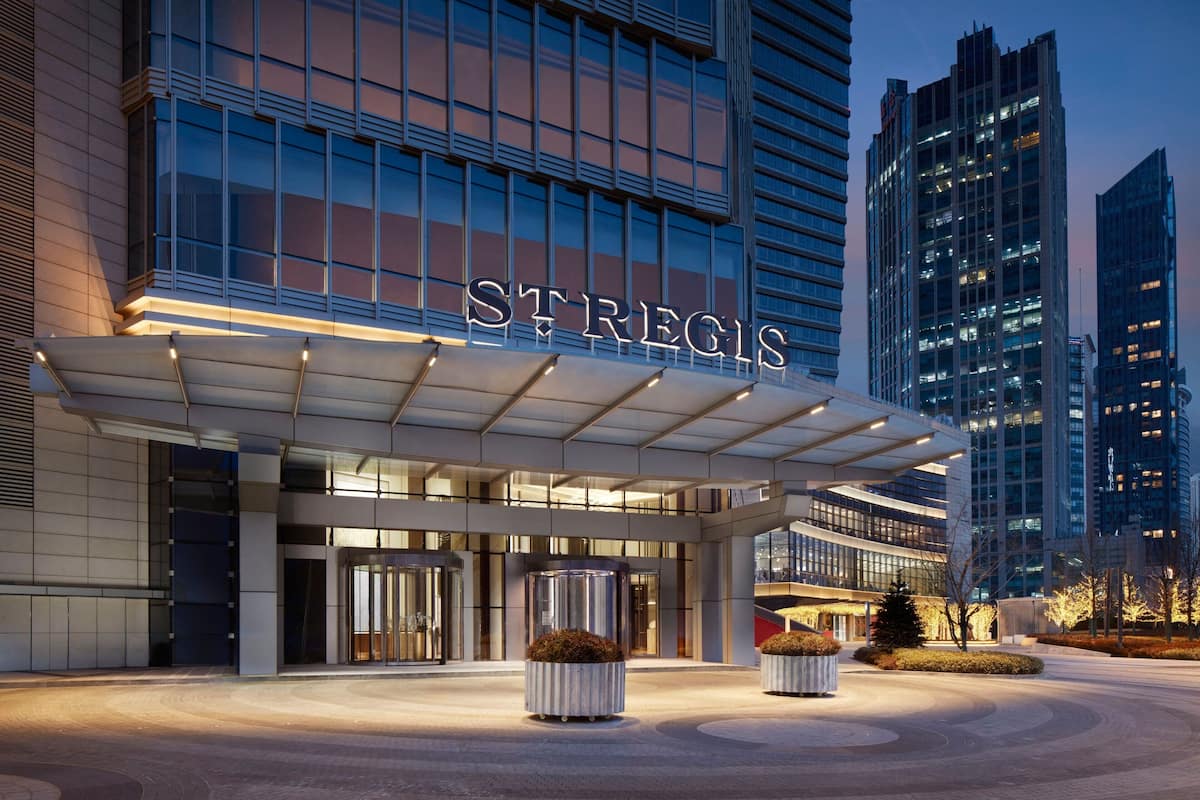 A modern hotel entrance with a prominent sign, large windows, and a well-lit facade.