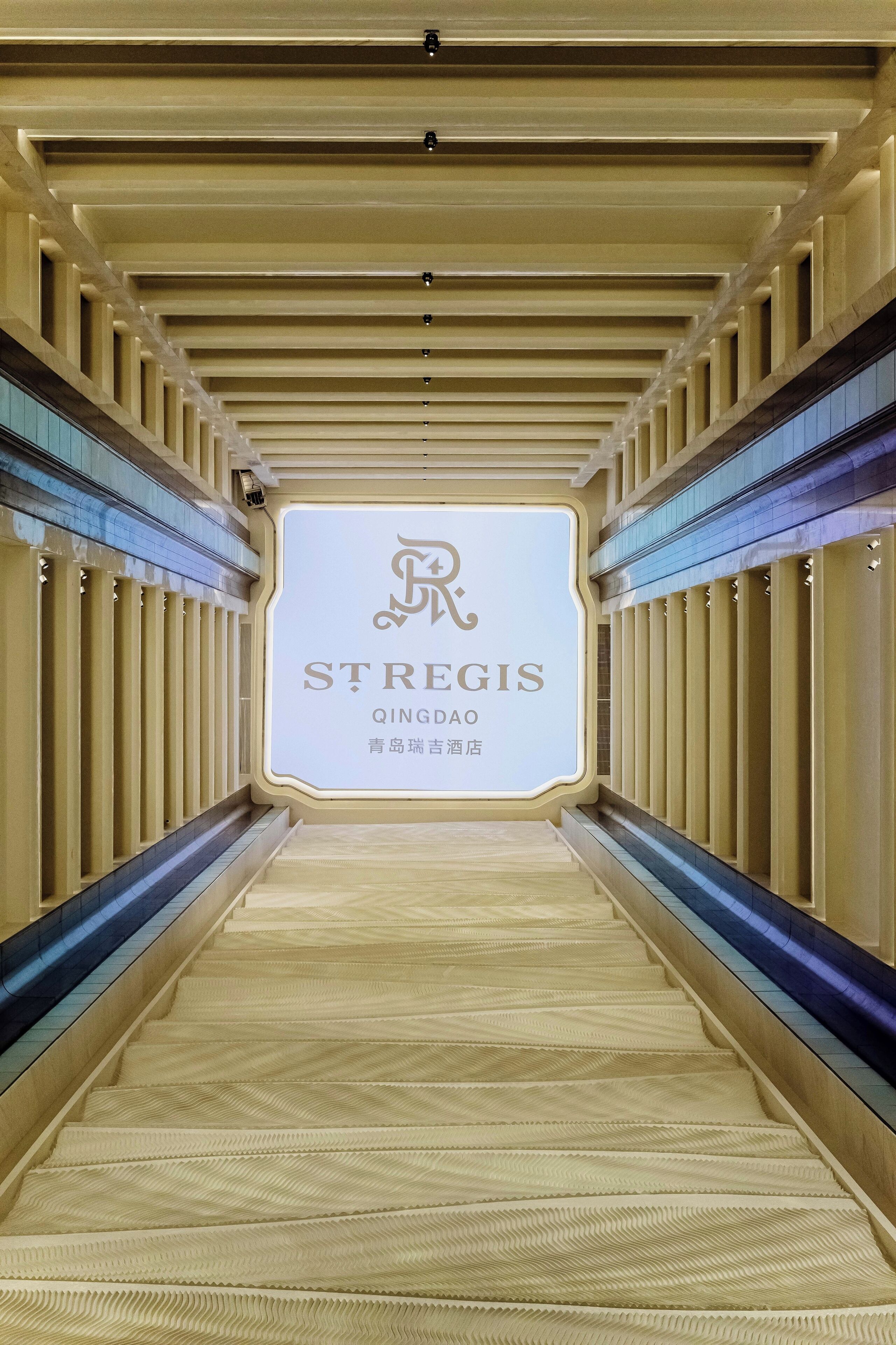 A corridor with a sign for St Regis Qingdao, featuring a modern design with a patterned floor and vertical light strips.