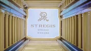 Un passadís amb un senyal per St Regis Qingdao, amb un disseny modern, un paviment amb dibuixos i tires de llum verticals.