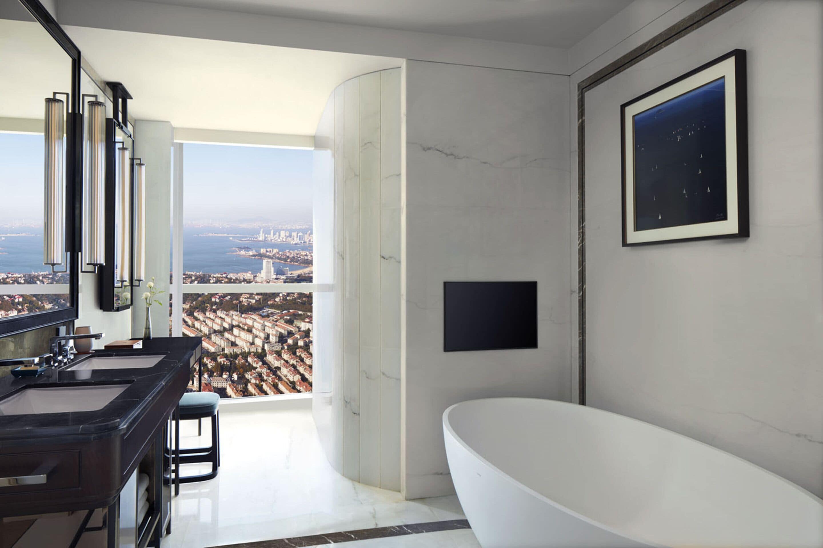 A modern bathroom with a large bathtub, a dual sink vanity, and a large window offering a city view.