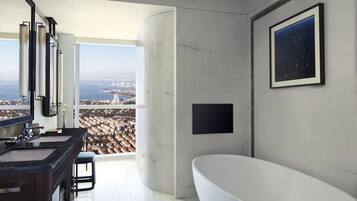 A modern bathroom with a large bathtub, a dual sink vanity, and a large window offering a city view.