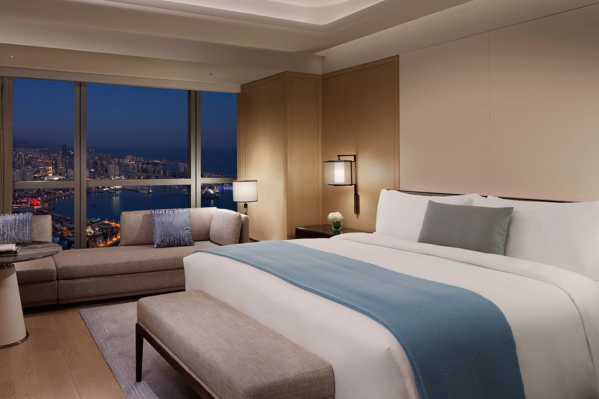 A hotel room with a large bed, a sofa, a desk, and a view of a cityscape at night.
