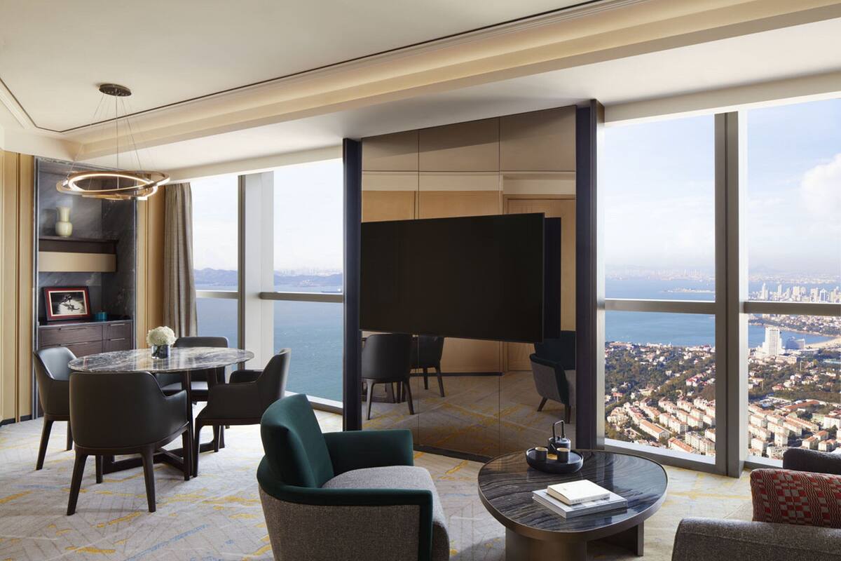 A spacious living room with a large window offering a city view, a flat-screen TV, and a dining area with chairs and a table.